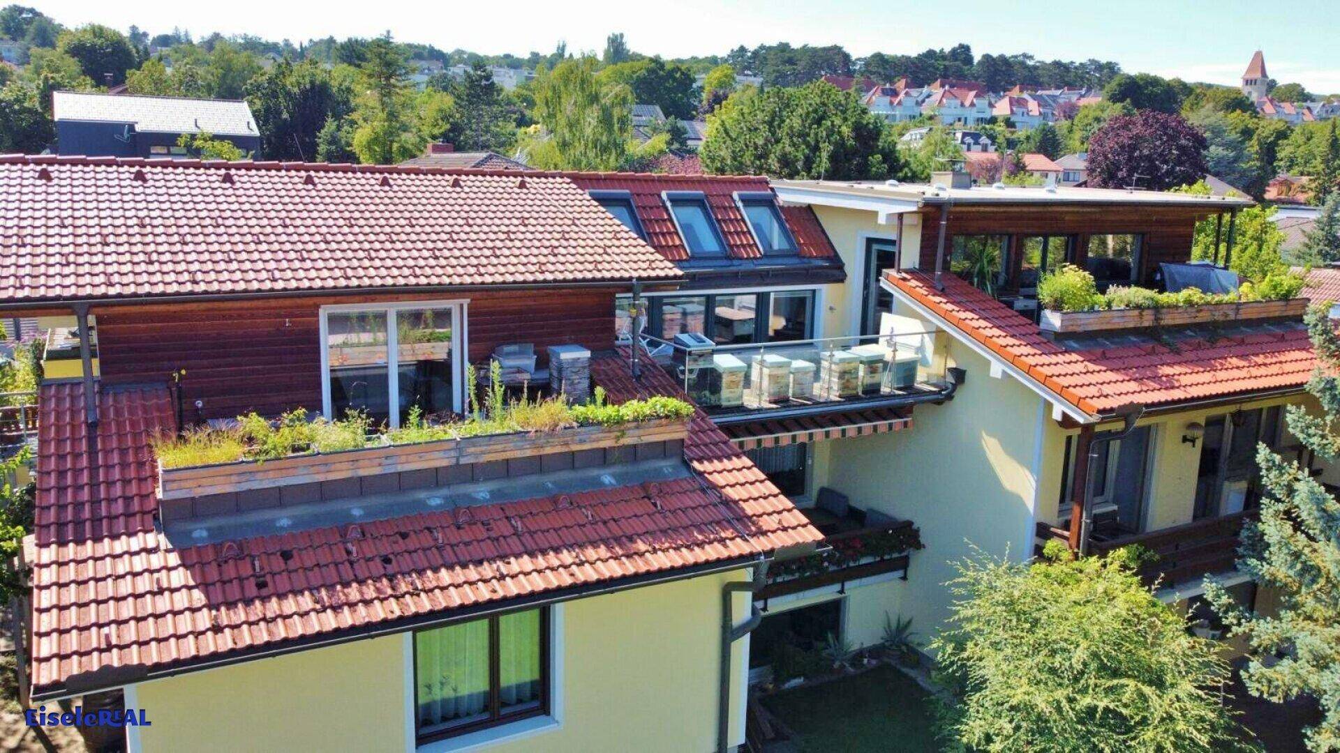 Luftaufnahme eines Wohnhauses mit mehreren Terrassen, roten Ziegeldächern und viel Grün.