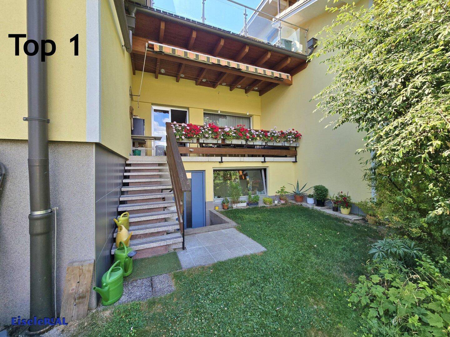 Außenansicht des Hauses mit Garten, Treppe zum Balkon und Kellerzugang.