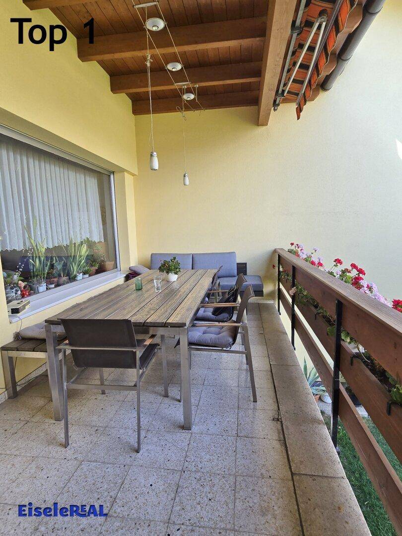 Überdachter Balkon mit Fliesenboden, Esstisch und bequemer Sitzgelegenheit.