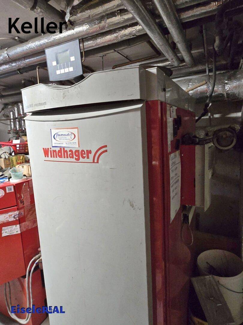 Heizraum im Keller mit einem Windhager-Heizsystem und sichtbaren Rohrleitungen an der Decke.