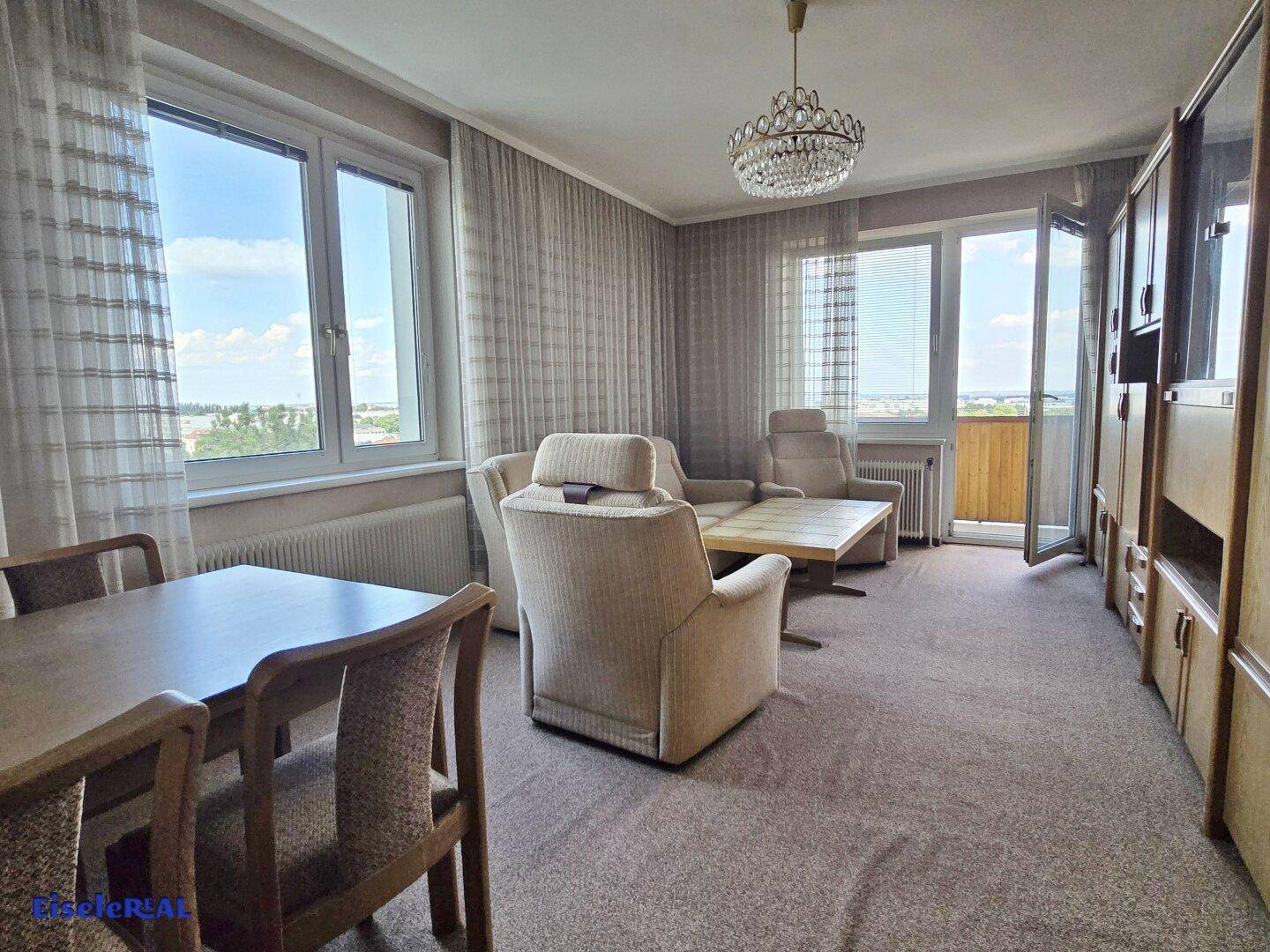Geräumiger Wohn- und Essbereich mit Teppichboden, großen Fenstern und Zugang zum Balkon.