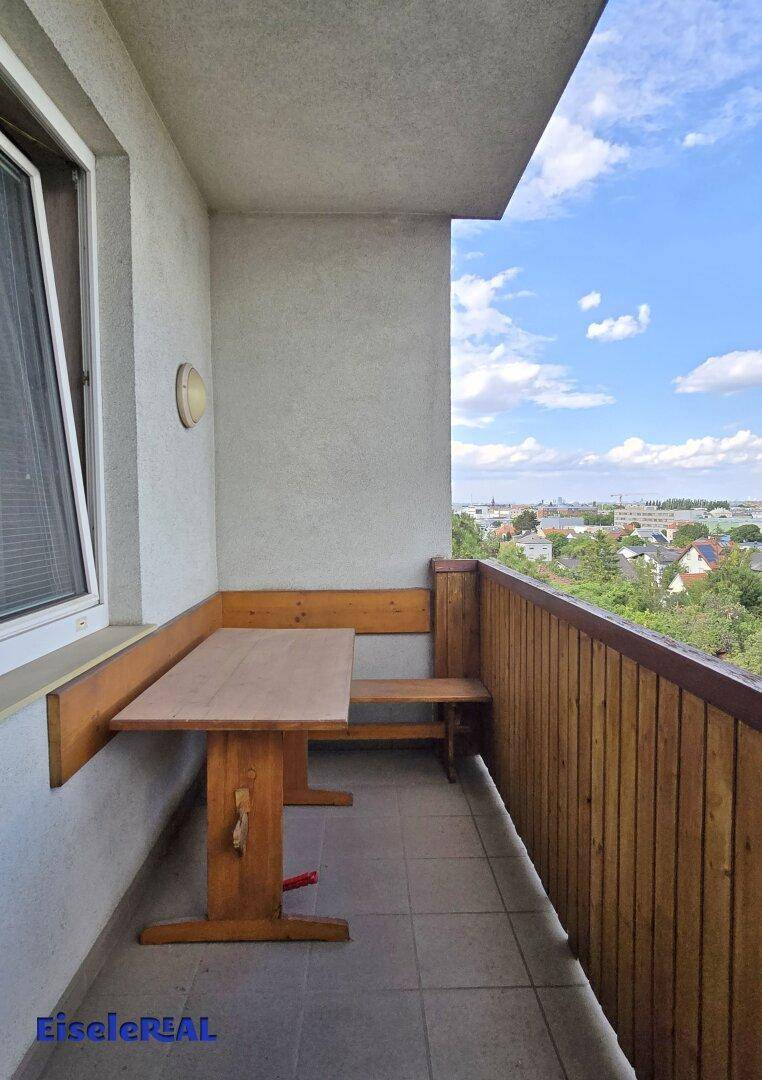 Gemütlicher Balkon mit Holztisch und Bänken, gefliestem Boden und weitem Ausblick.