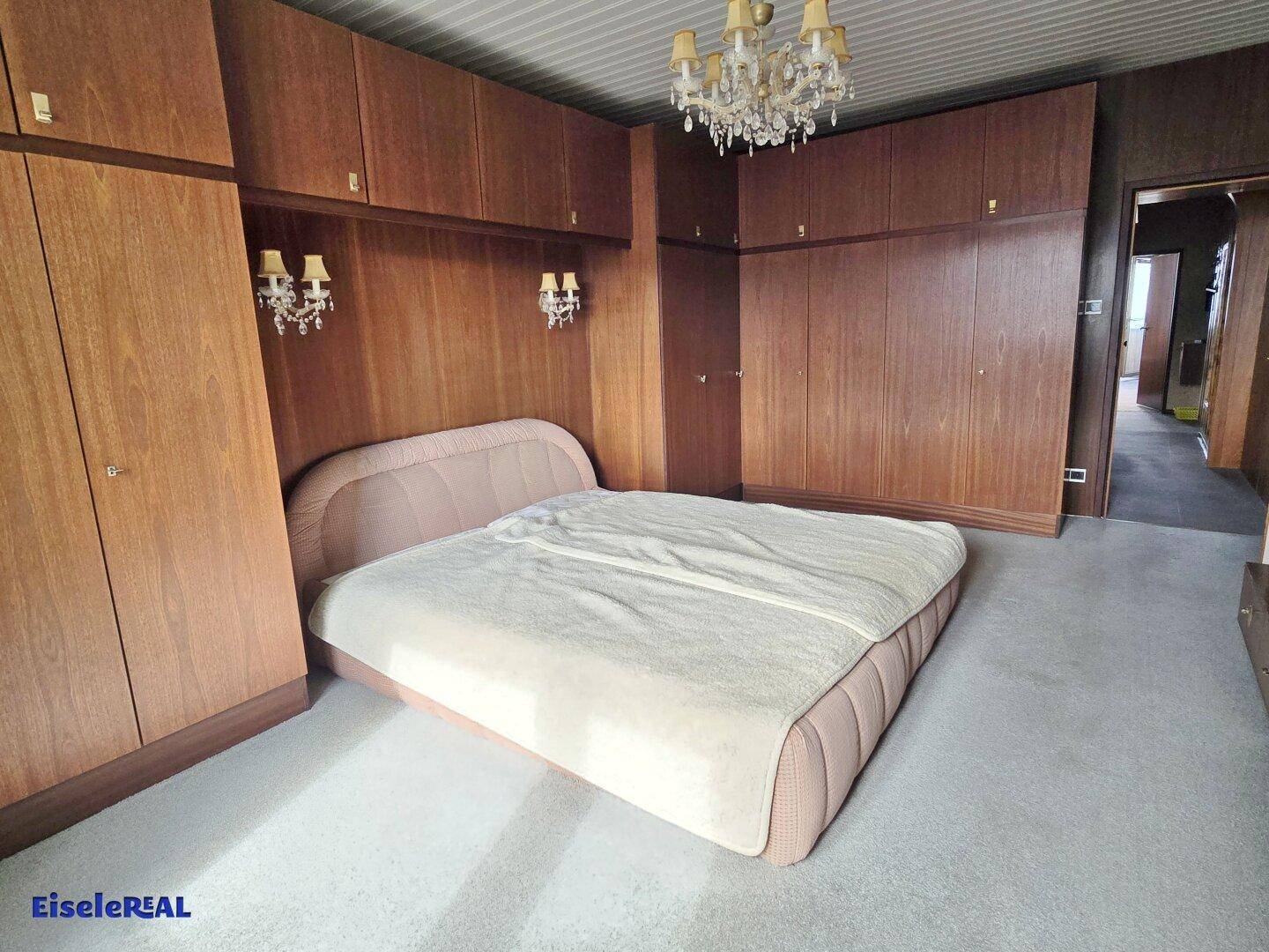 Schlafzimmer mit großem Bett, Einbauschränken aus Holz und Teppichboden.