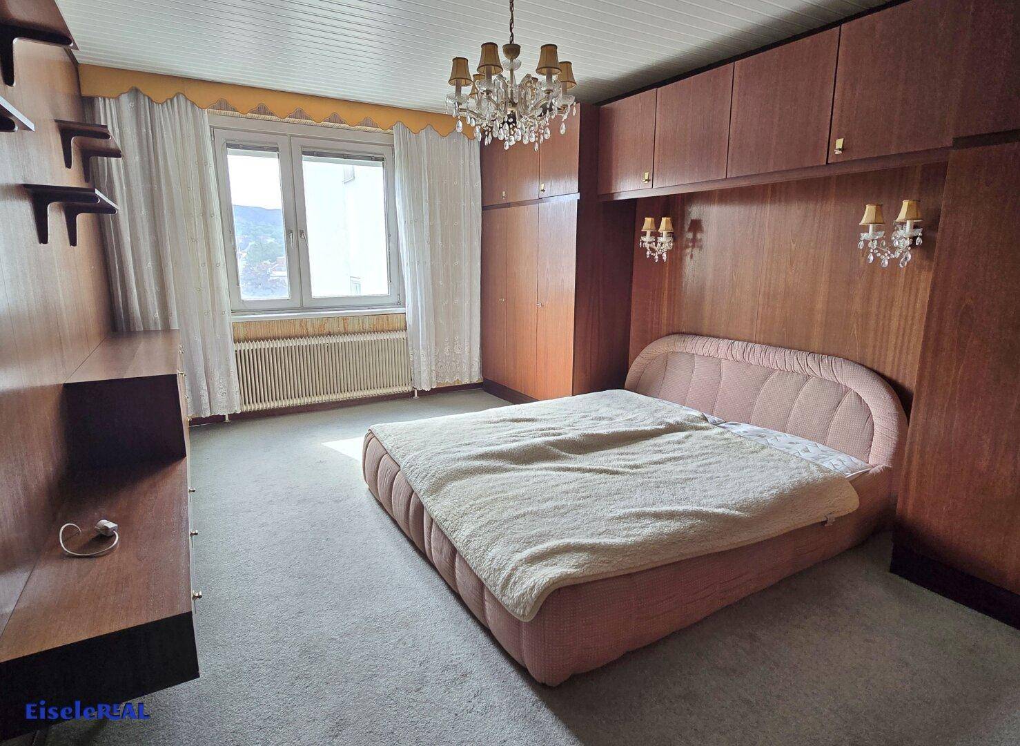 Helles Schlafzimmer mit Teppichboden, Einbauschränken und Fenster mit Blick ins Grüne.