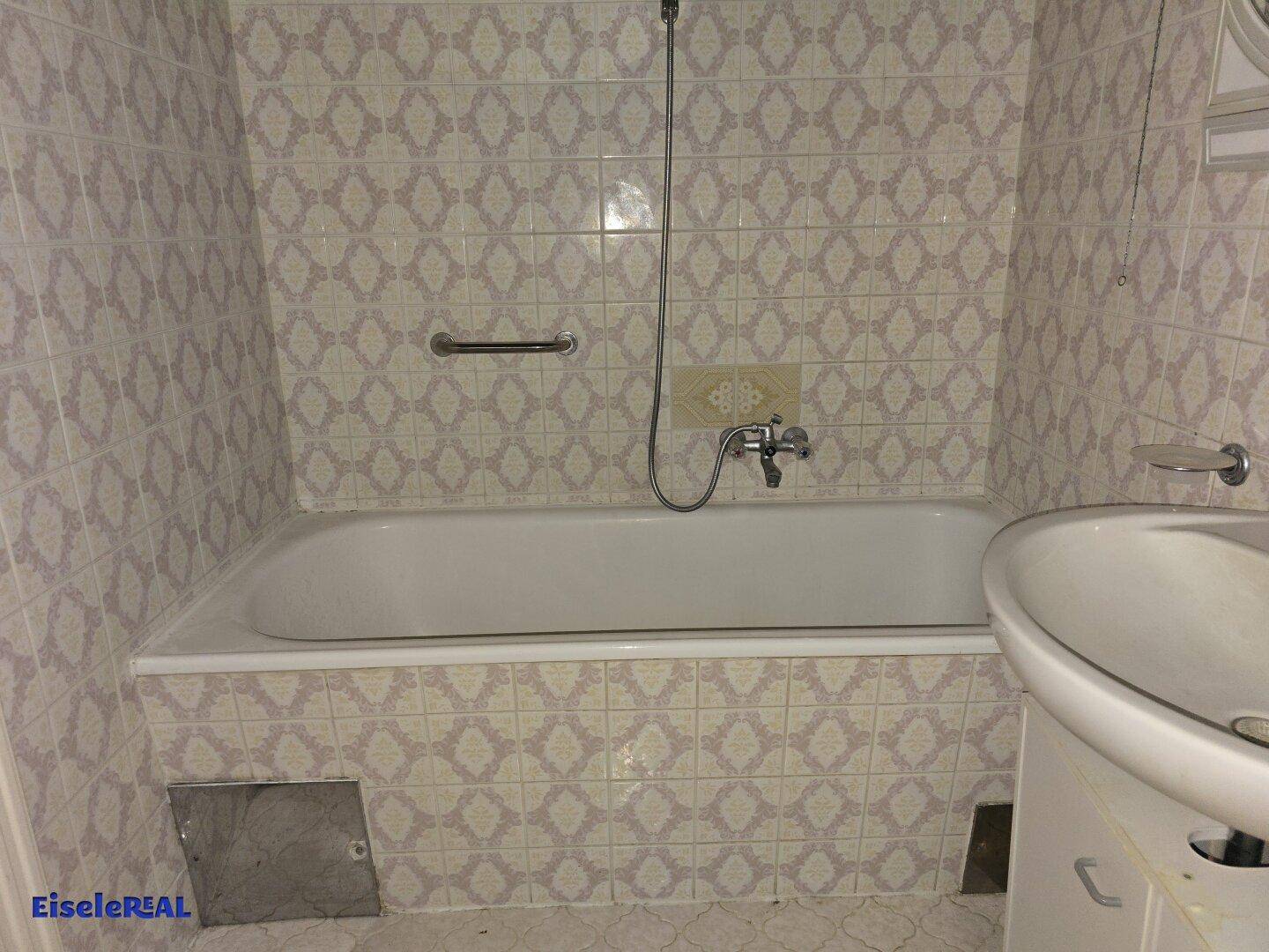 Badezimmer mit Badewanne, Waschbecken und Fliesen im 80er-Jahre-Stil.