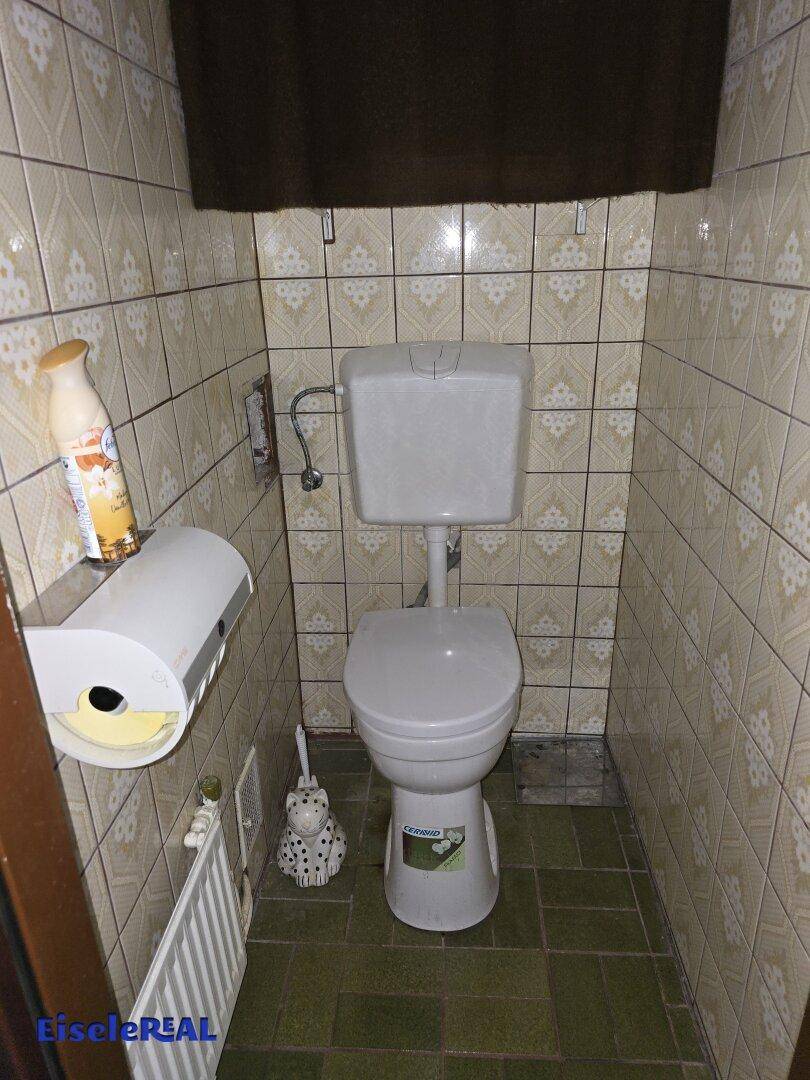 Separate Toilette mit WC, Heizung und Fliesen im 80er-Jahre-Stil.