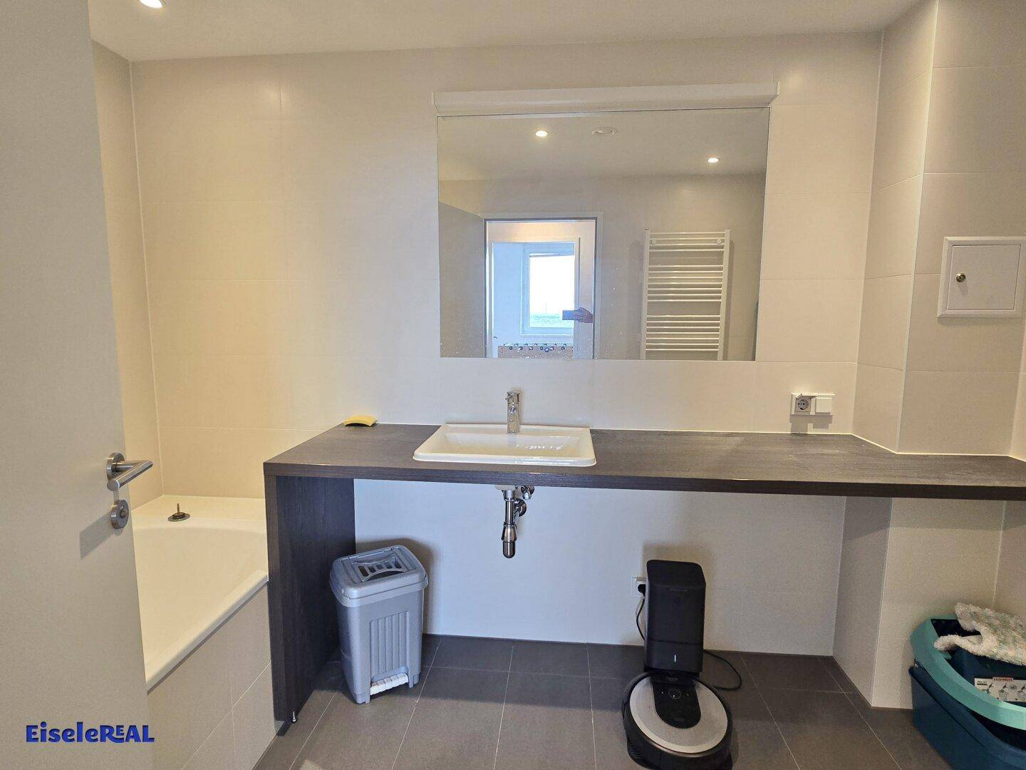 Modernes Badezimmer mit großem Waschtisch, Spiegel und einer Badewanne, hell gefliest.