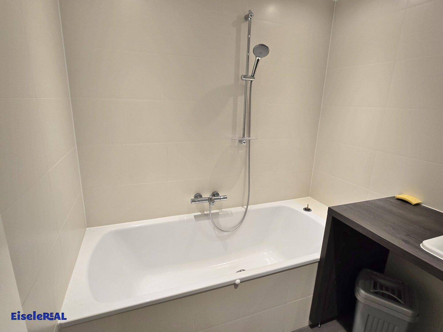 Badewanne mit Duscharmatur in einem hell gefliesten Badezimmer, sauber und funktional.