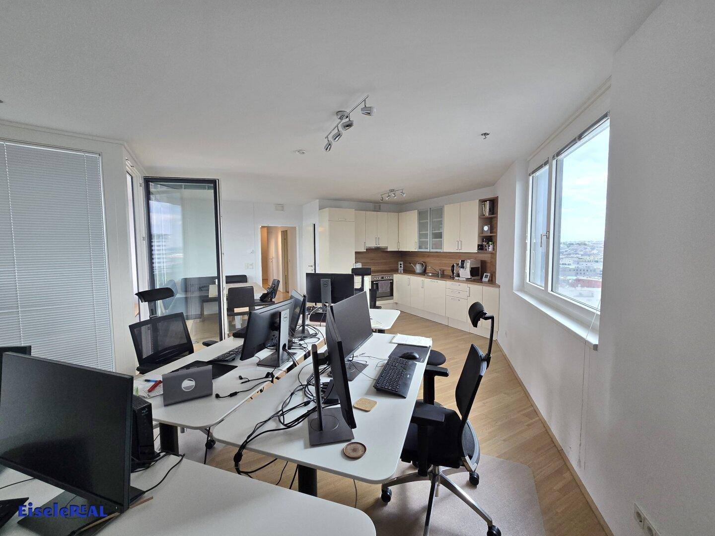 Großzügiger Bürobereich mit mehreren Arbeitsplätzen und integrierter Küchenzeile im Hintergrund.