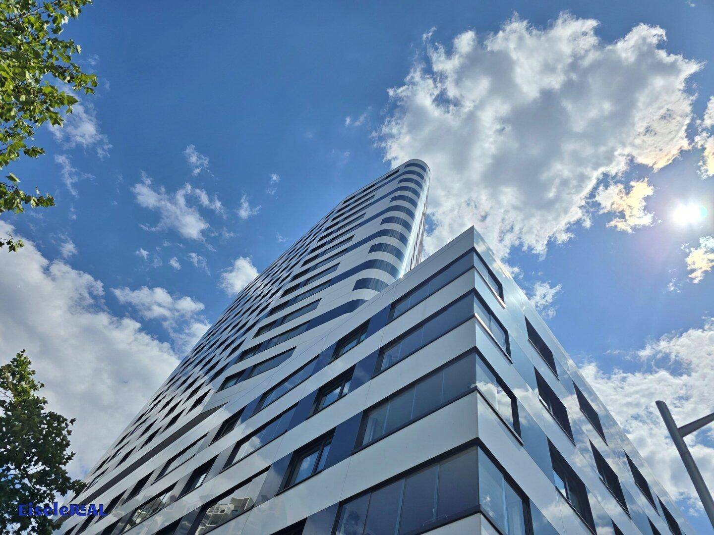 Modernes Hochhaus mit reflektierender Fassade unter sonnigem Himmel mit Wolken.