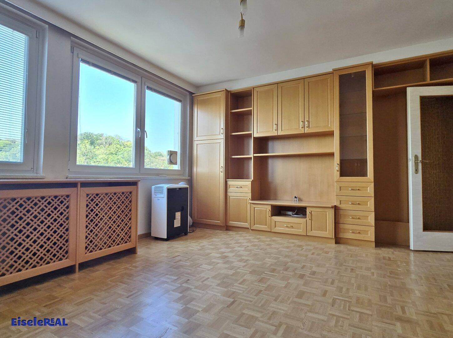 Geräumiges Wohnzimmer mit Holzschränken, Parkettboden und viel Tageslicht.