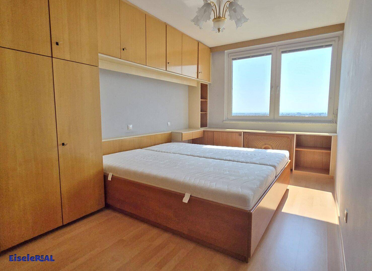 Schlafzimmer mit Doppelbett, Einbauschränken und hellen Fenstern.