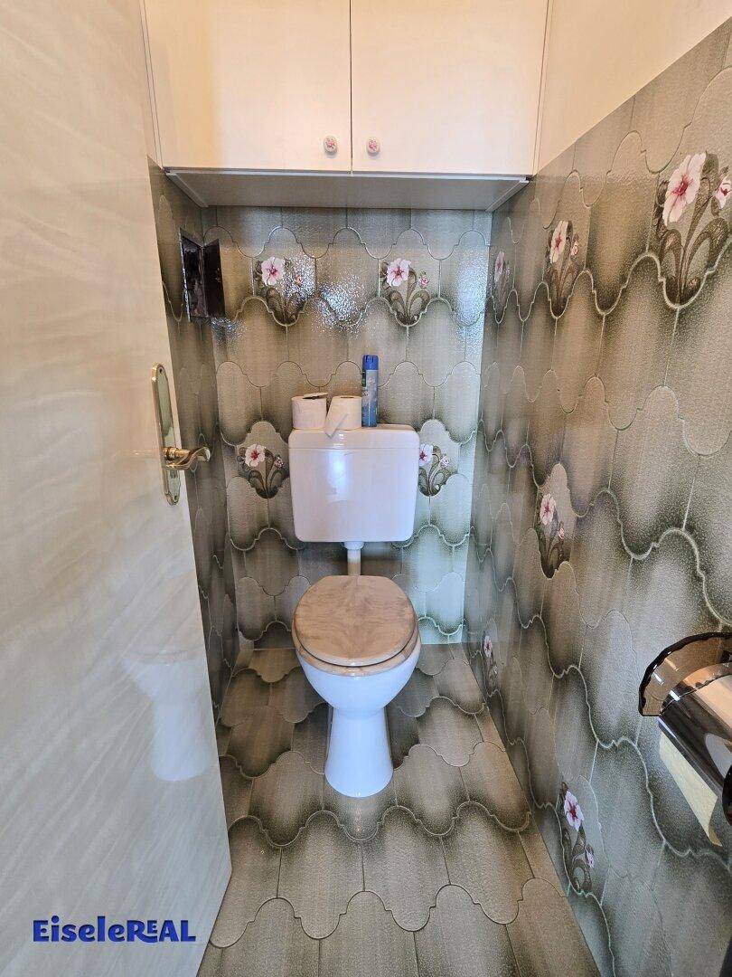 Separate Toilette mit floral gemusterten Fliesen und Stauraum.