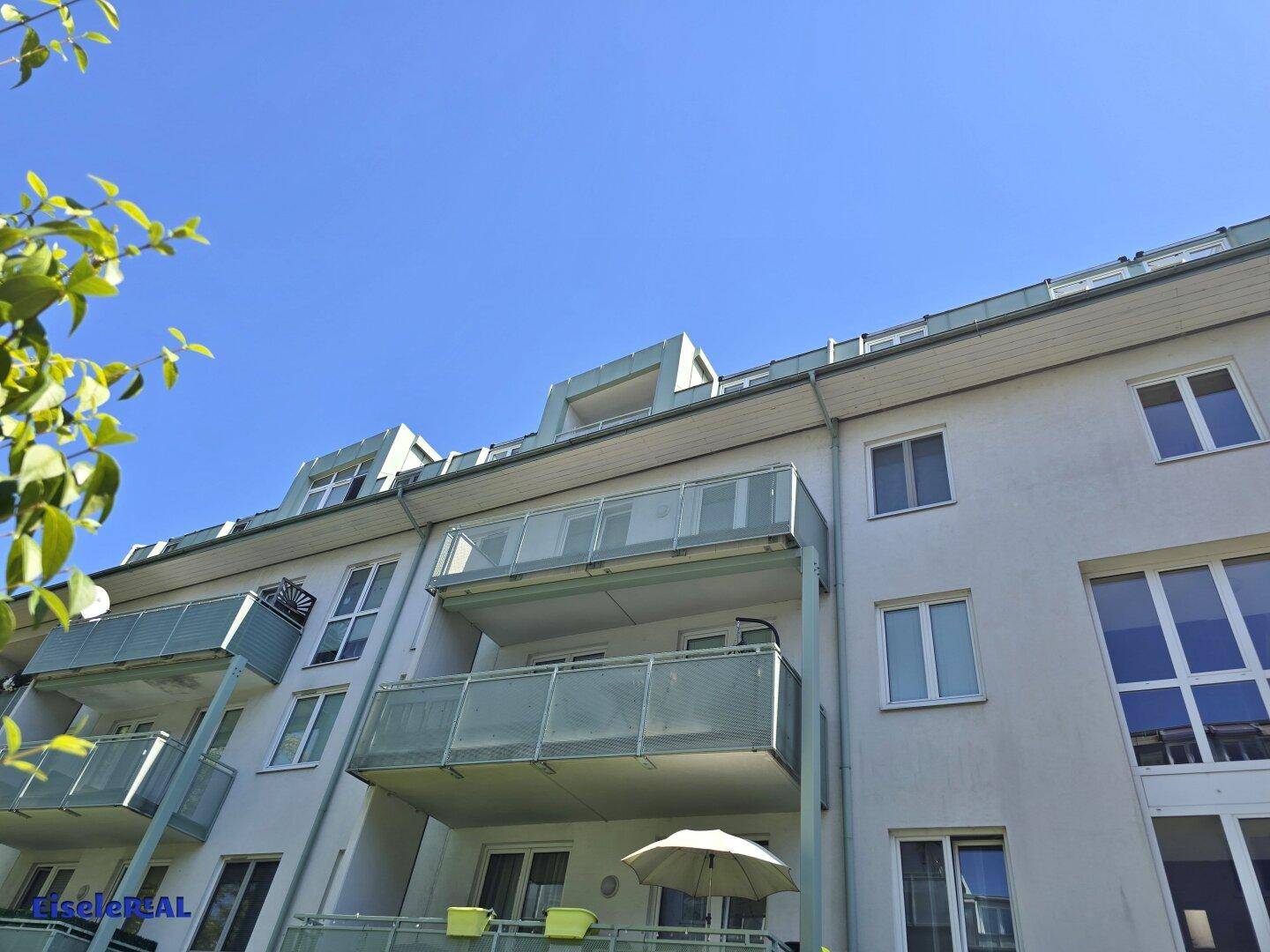 Fassade eines modernen Wohngebäudes mit mehreren Balkonen und großen Fenstern unter blauem Himmel.