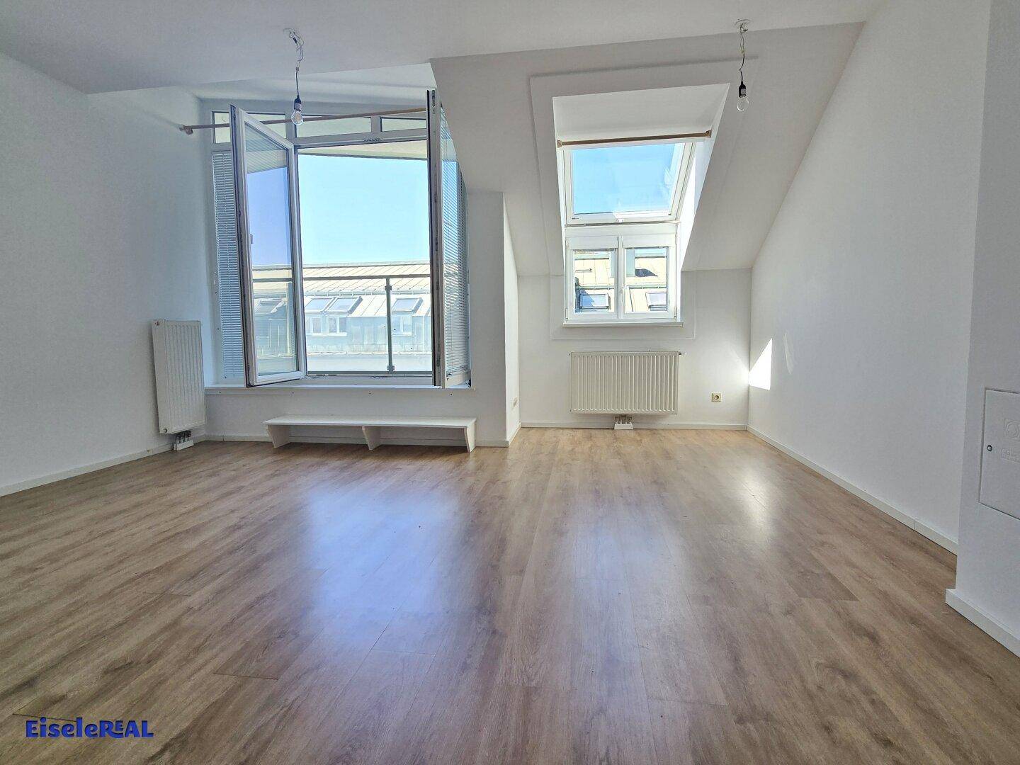 Geräumiges Wohnzimmer mit Laminatboden, großen Fenstern und einem Dachfenster für viel Helligkeit.