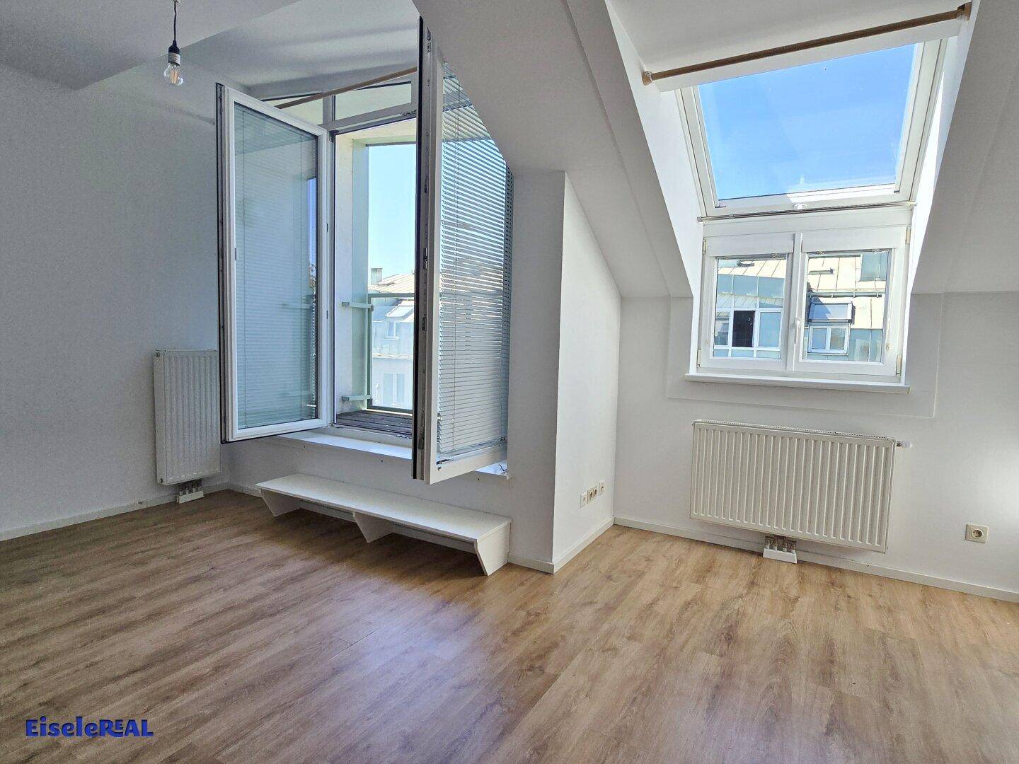 Helles Wohnzimmer mit Laminatboden, einem großen Fenster und einem Dachfenster, das den Raum erhellt.