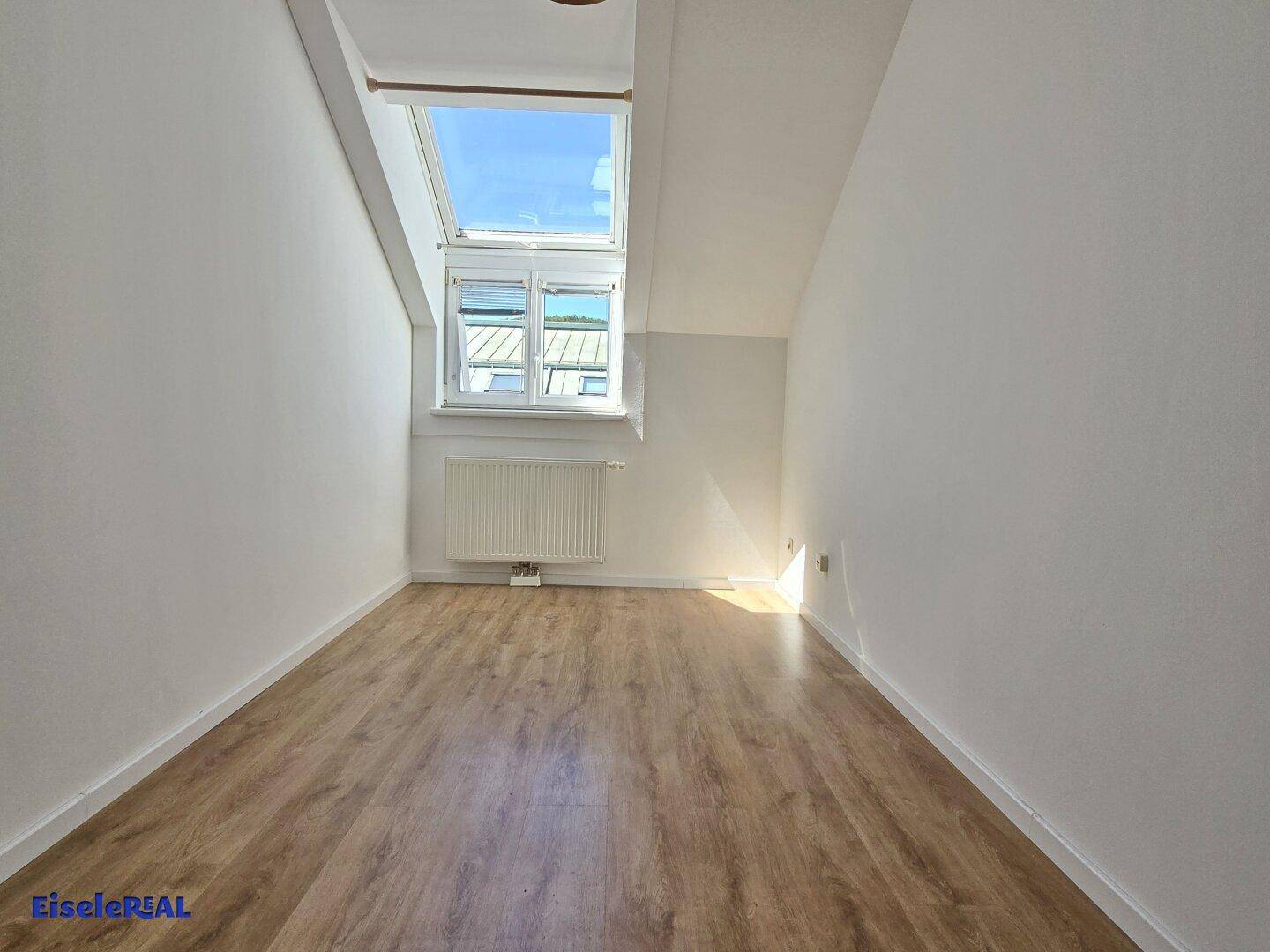 Helles Schlafzimmer mit Dachschräge, Laminatboden und großem Dachfenster für viel Licht.