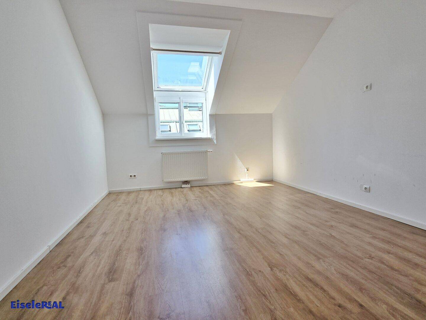 Geräumiges Schlafzimmer mit Dachschräge, Laminatboden und einem großen Dachfenster.