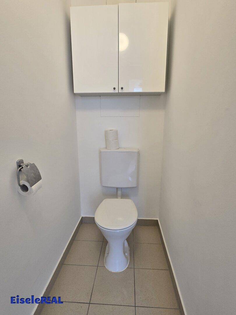 Separates WC mit Toilette, Waschbecken und Hängeschrank, in schlichtem Design.