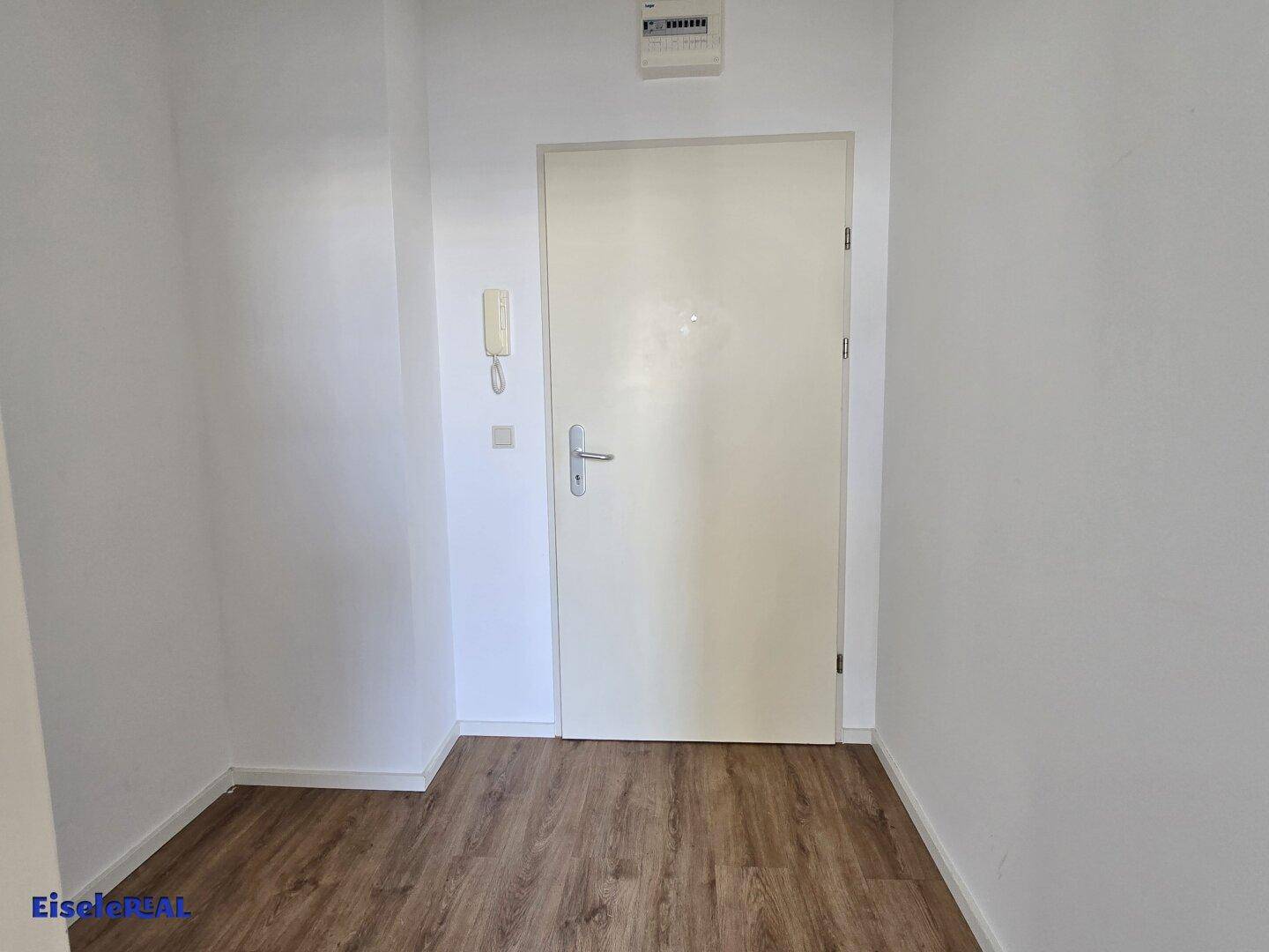 Heller Eingangsbereich mit Holzboden und weißer Tür, bereit für die individuelle Gestaltung.