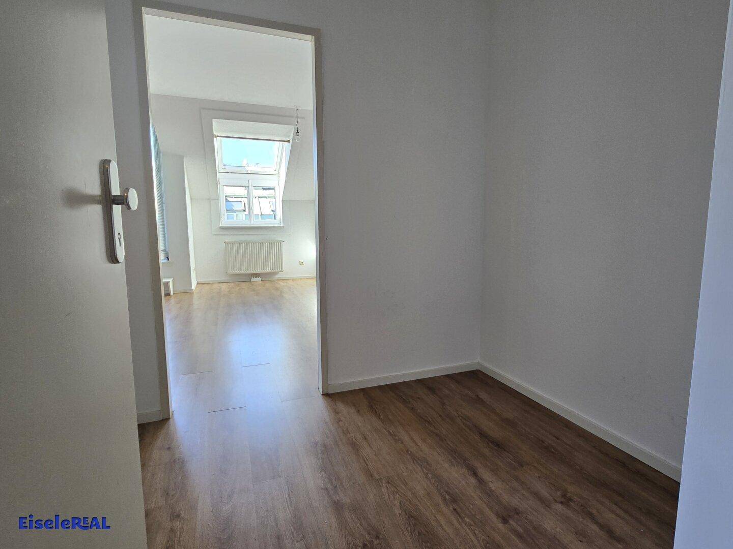 Blick vom Flur in einen hellen Raum mit Dachfenster und Laminatboden, der viel Tageslicht bietet.