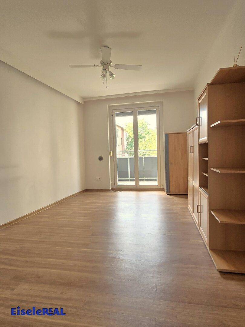 Helles Wohnzimmer mit Laminatboden, Deckenventilator und Zugang zum Balkon.