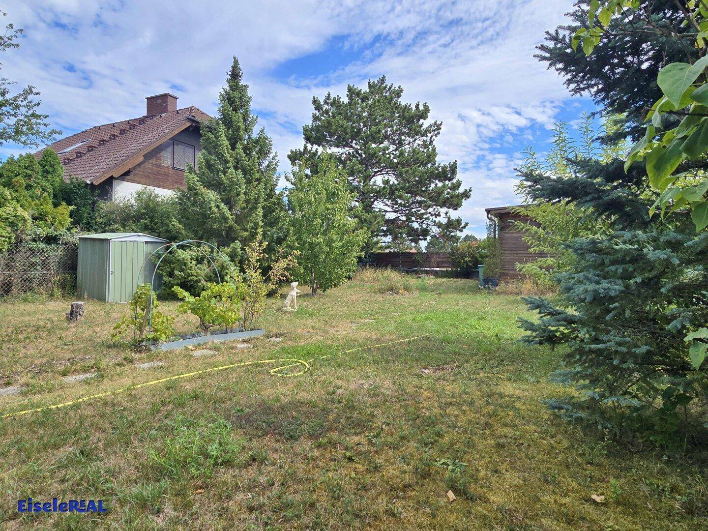 Großer Garten mit Rasenfläche, einem Geräteschuppen und einem Wohnhaus im Hintergrund.