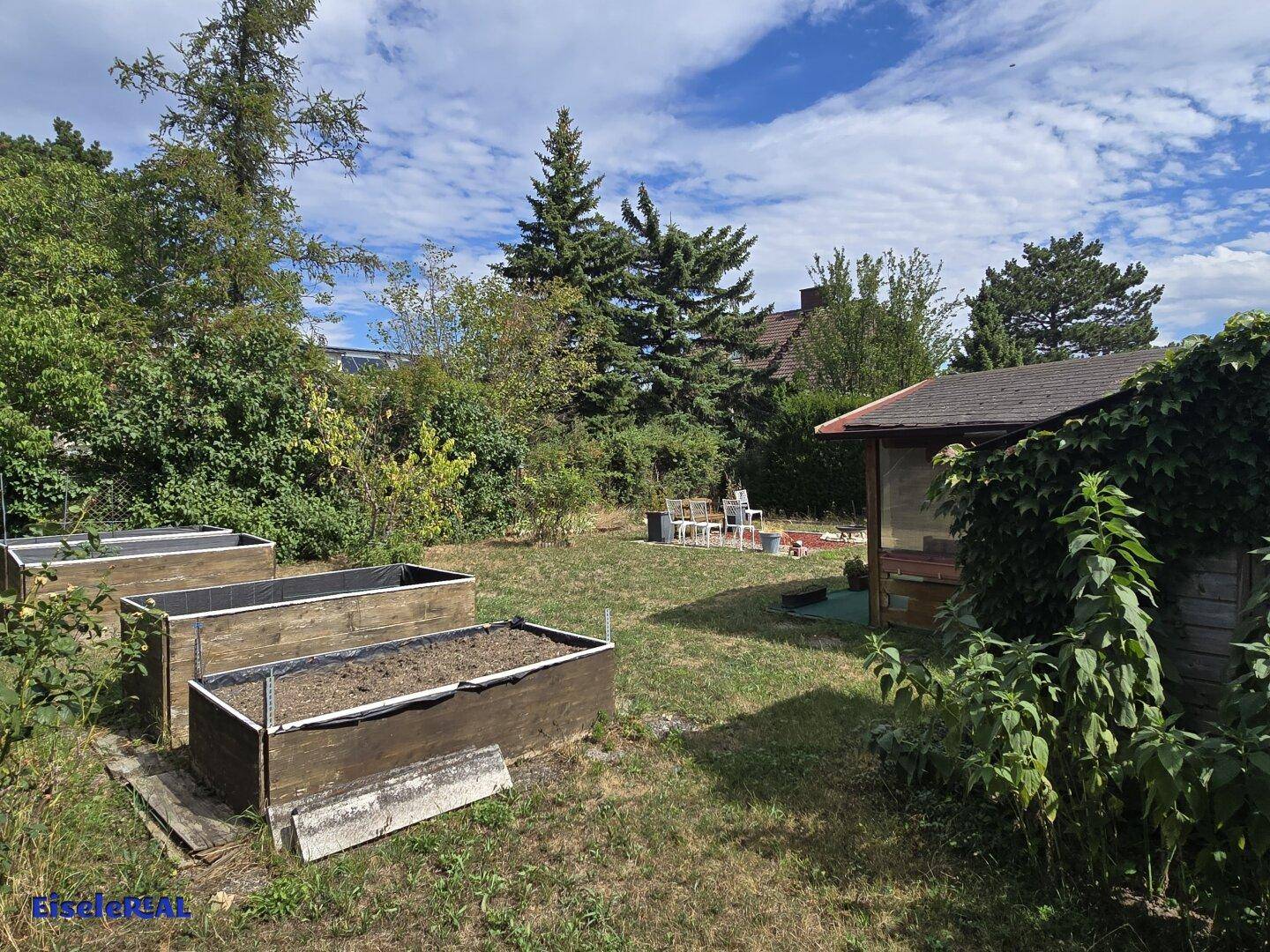 Gartenbereich mit Hochbeeten für den Anbau und einem kleinen Holzschuppen im Hintergrund.