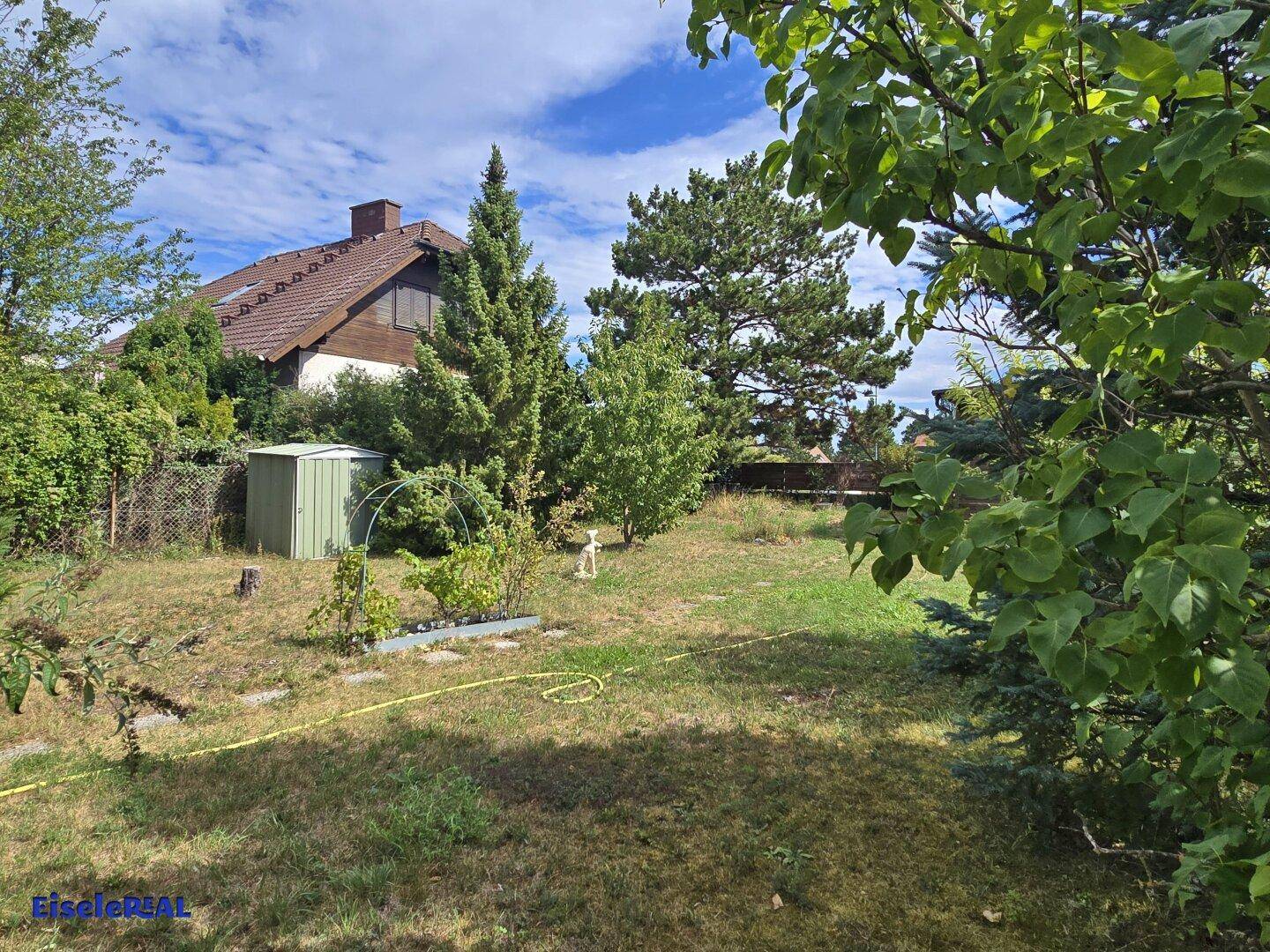 Großer Garten mit Rasenfläche, einem Geräteschuppen und einem Wohnhaus im Hintergrund.