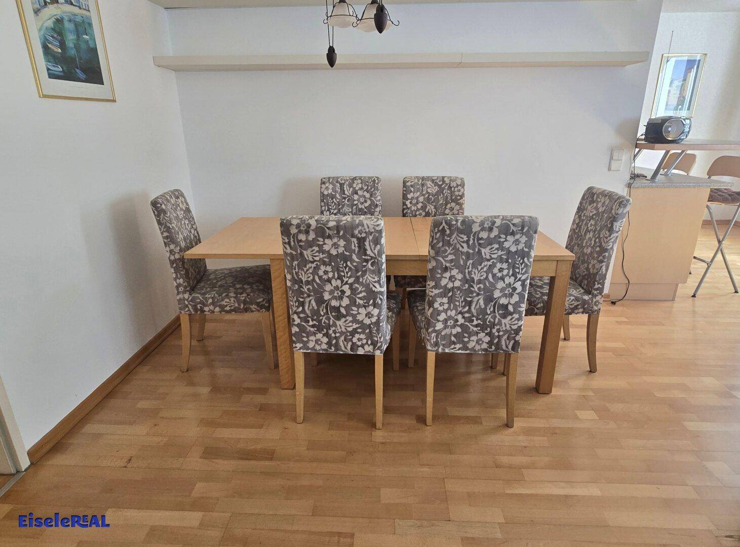 Heller Essbereich mit Holztisch und sechs gepolsterten Stühlen auf Parkettboden.