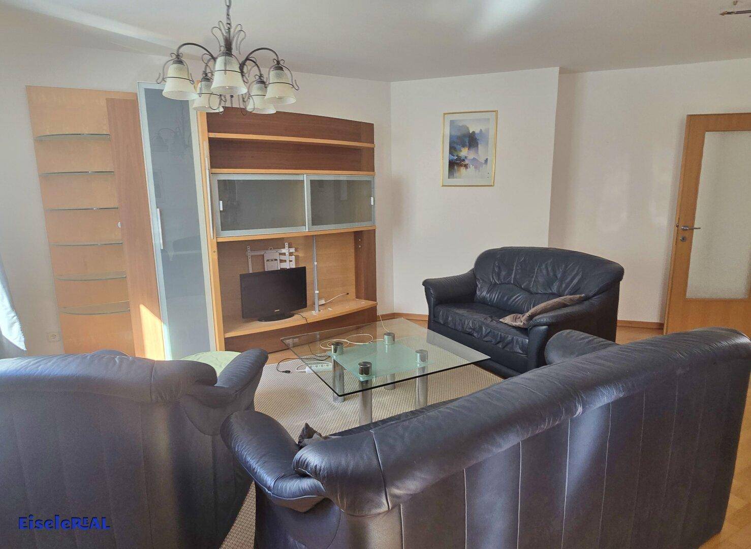 Gemütliches Wohnzimmer mit dunklen Ledersofas, Couchtisch und Wandregal.