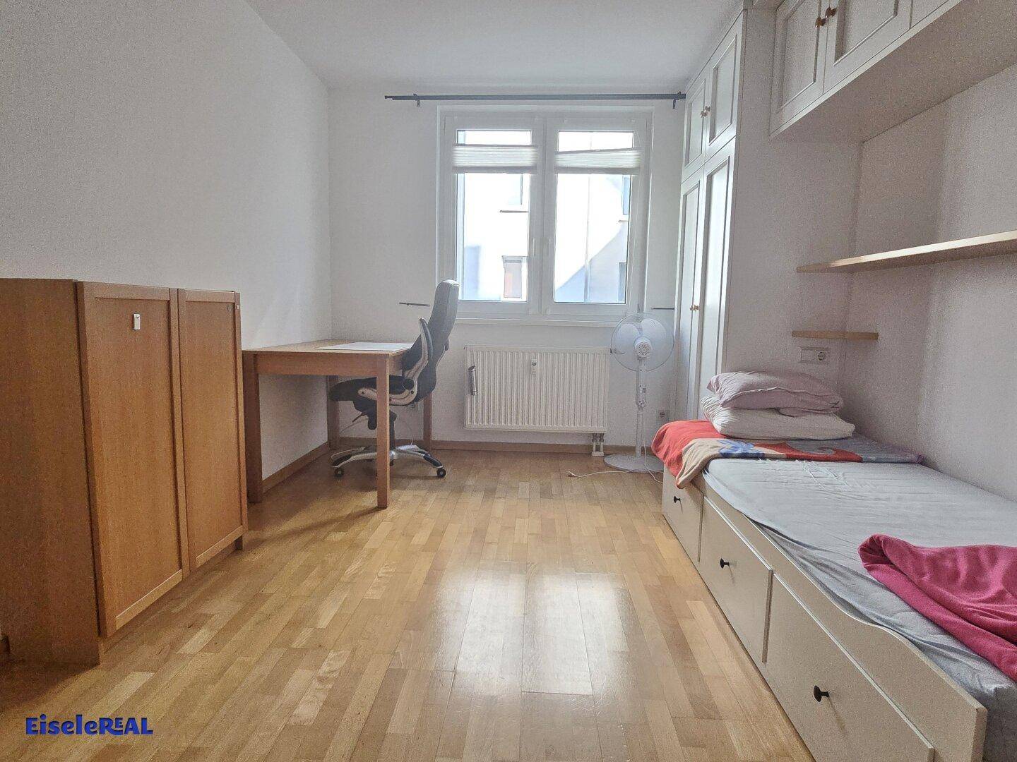 Helles Schlafzimmer mit Einzelbett, Schreibtisch und Einbauschränken.