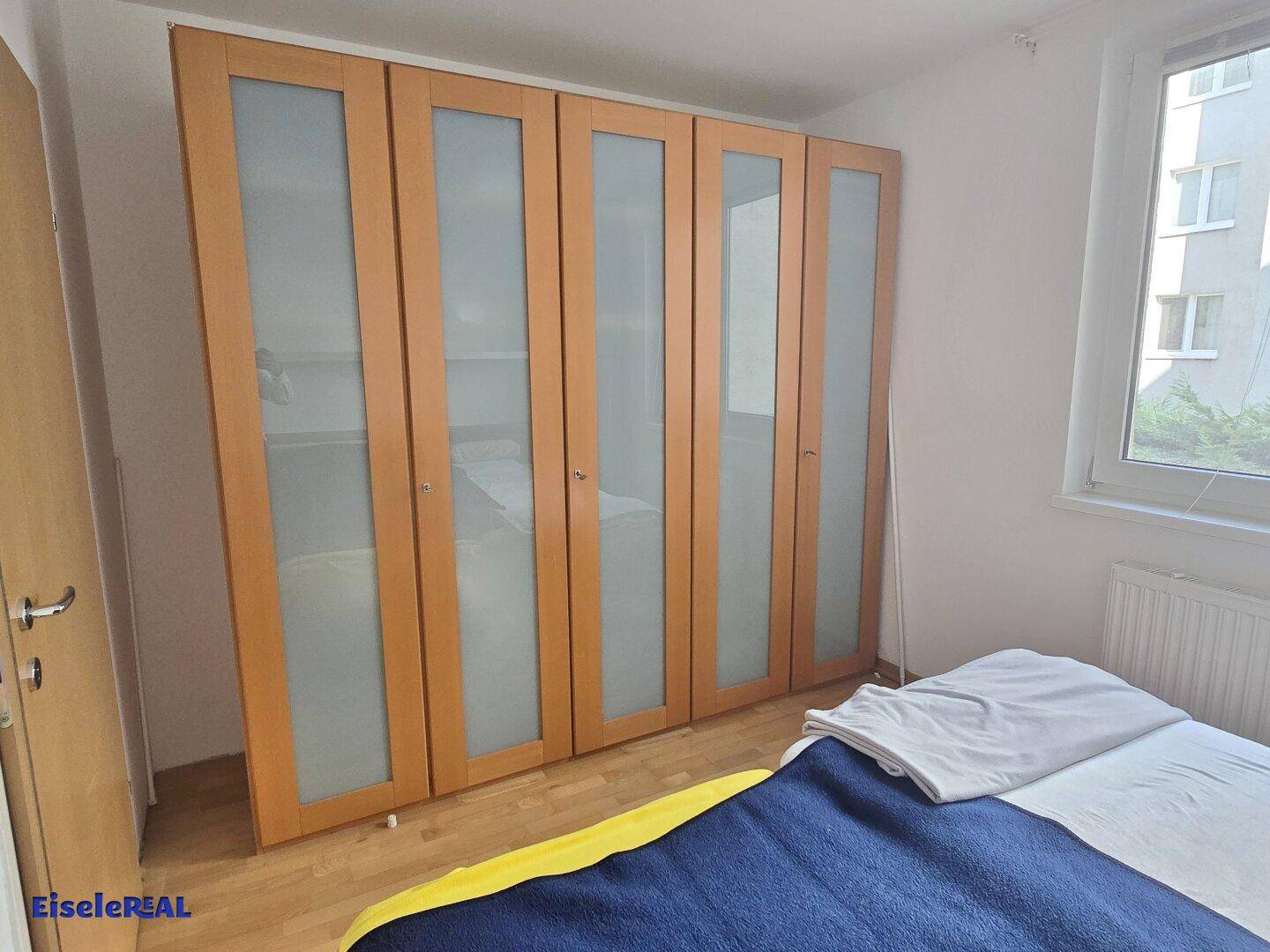 Schlafzimmer mit großem Kleiderschrank mit Milchglasfronten und Parkettboden.
