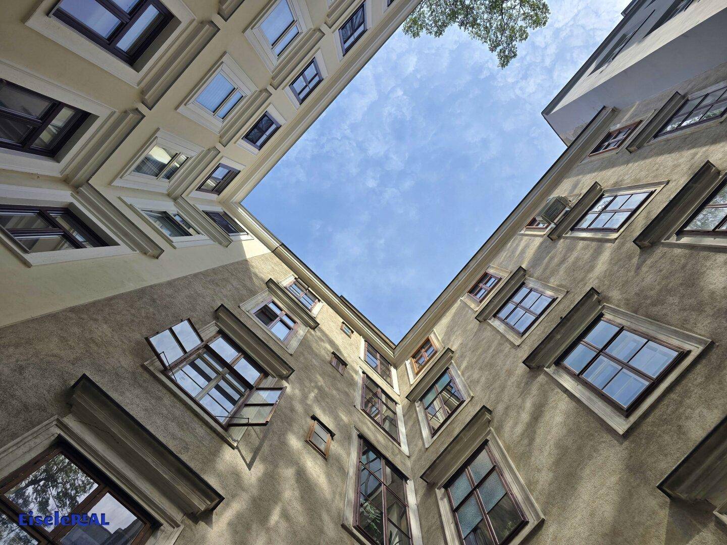 Blick in einen Innenhof eines Altbaus mit vielen Fenstern und blauem Himmel.