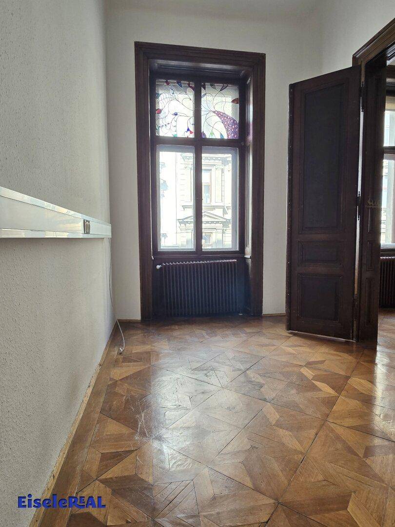 Zimmer mit einzigartigem Parkettboden, einem Fenster mit Buntglasdetails und Heizkörper.