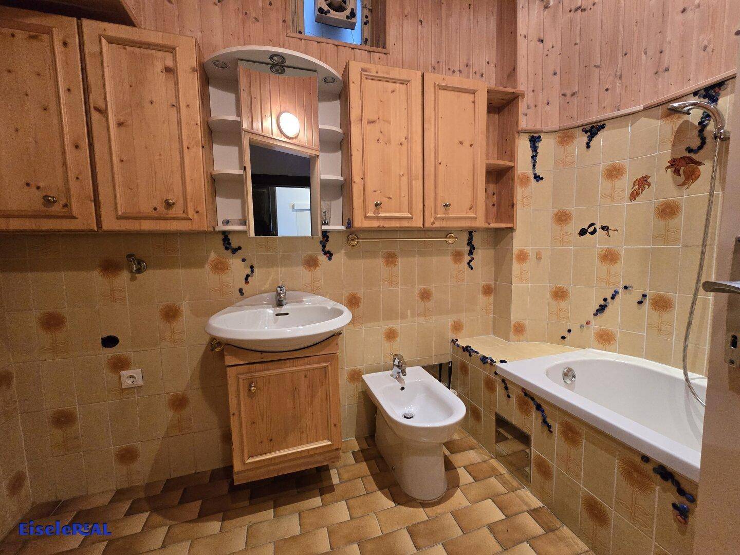 Badezimmer mit Holzverkleidung, gefliestem Boden, Waschbecken, Bidet und Badewanne.
