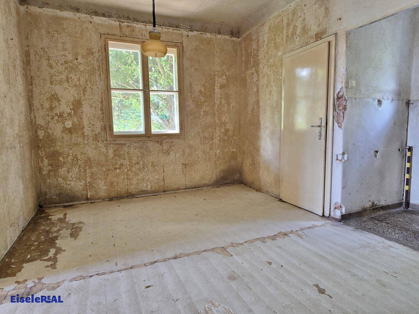 Renovierungsbedürftiger Raum mit abgenutzten Wänden und einem Fenster, das Tageslicht hereinlässt.