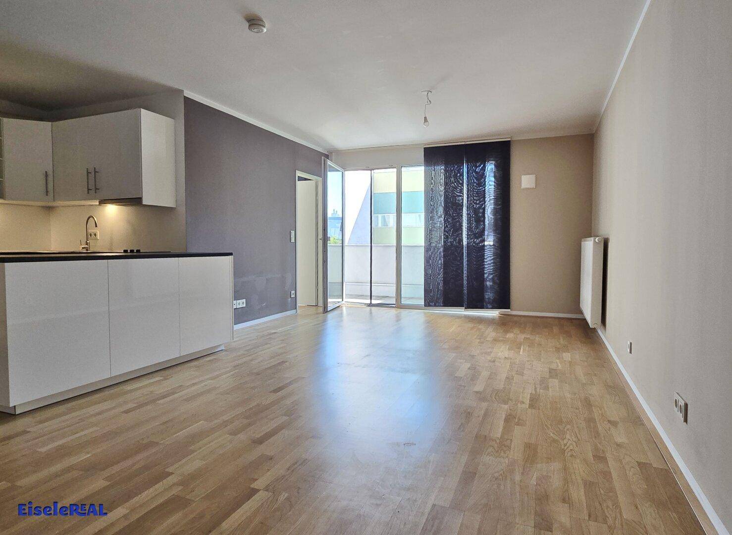 Offener Wohnbereich mit integrierter Küchenzeile und Zugang zu einem Balkon.