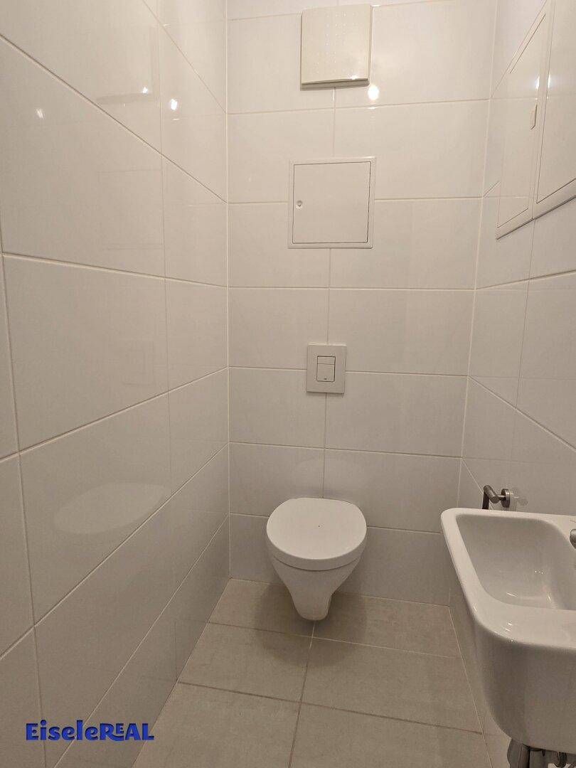 Kleines Gäste-WC mit weißen Fliesen, wandhängendem WC und Handwaschbecken.