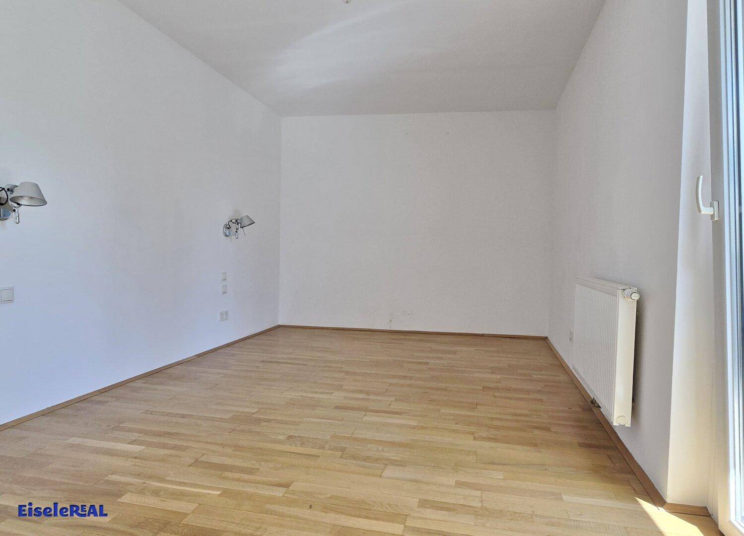 Helles Schlafzimmer mit Holzboden und weißen Wänden, bereit zur individuellen Gestaltung.