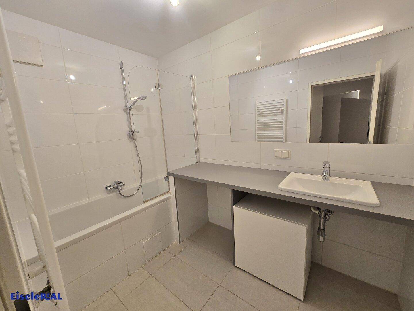 Modernes Badezimmer mit Badewanne, Waschtisch, großem Spiegel und Handtuchheizkörper.