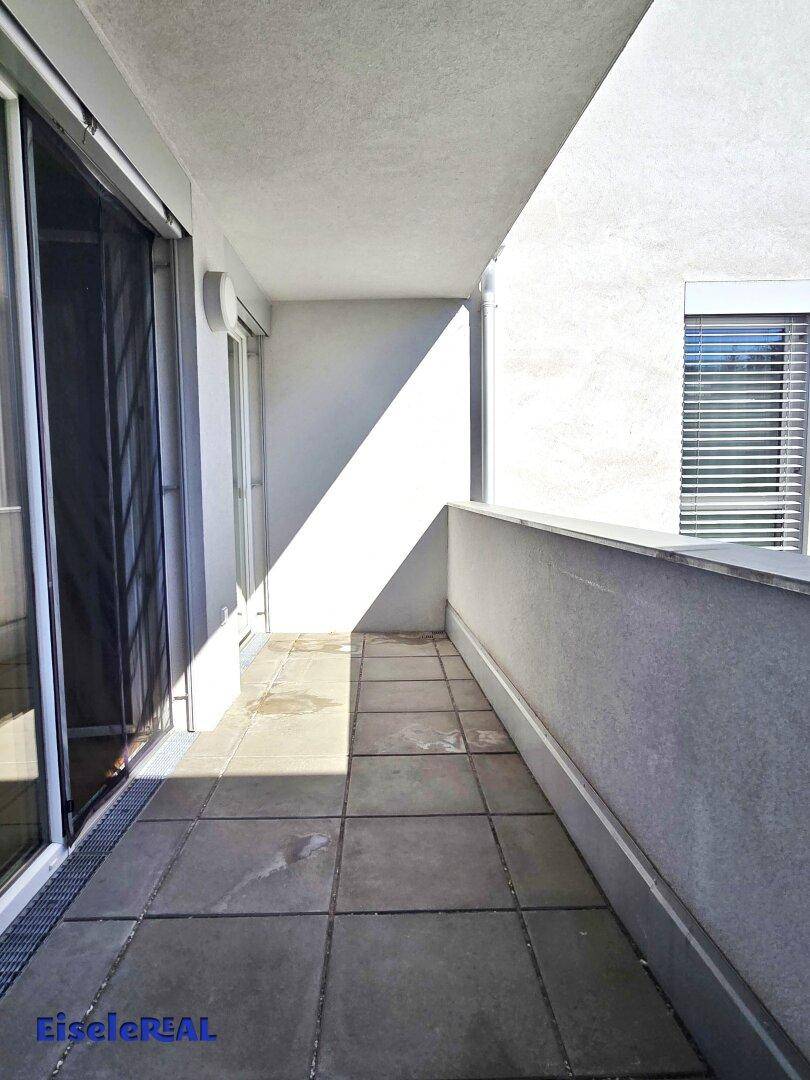 Heller Balkon mit Fliesenboden und Zugang zum Innenbereich, teilweise sonnig.
