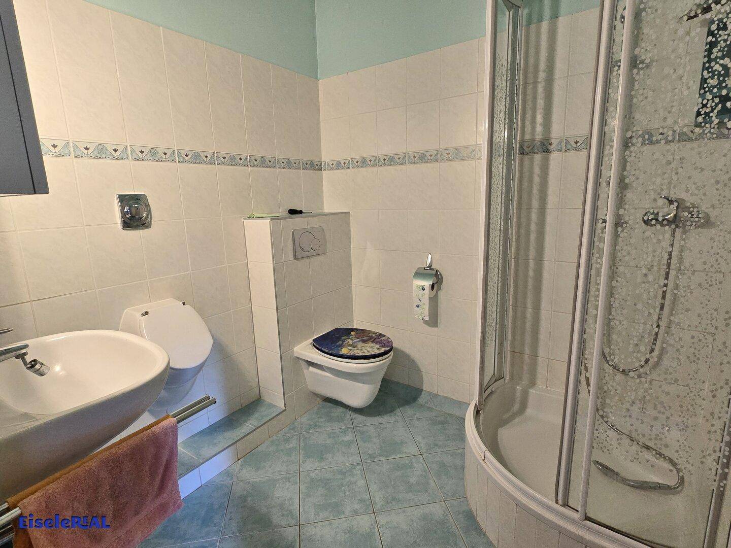 Badezimmer mit Dusche, wandhängendem WC und modernem Waschbecken in hellen Farben.