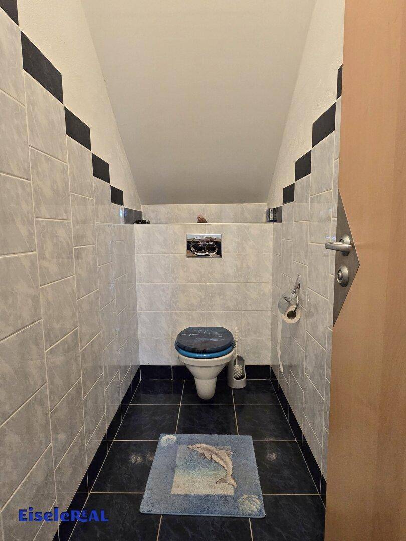 Kleines Gäste-WC mit dunklen Fliesen, WC und geometrischem Wanddesign.