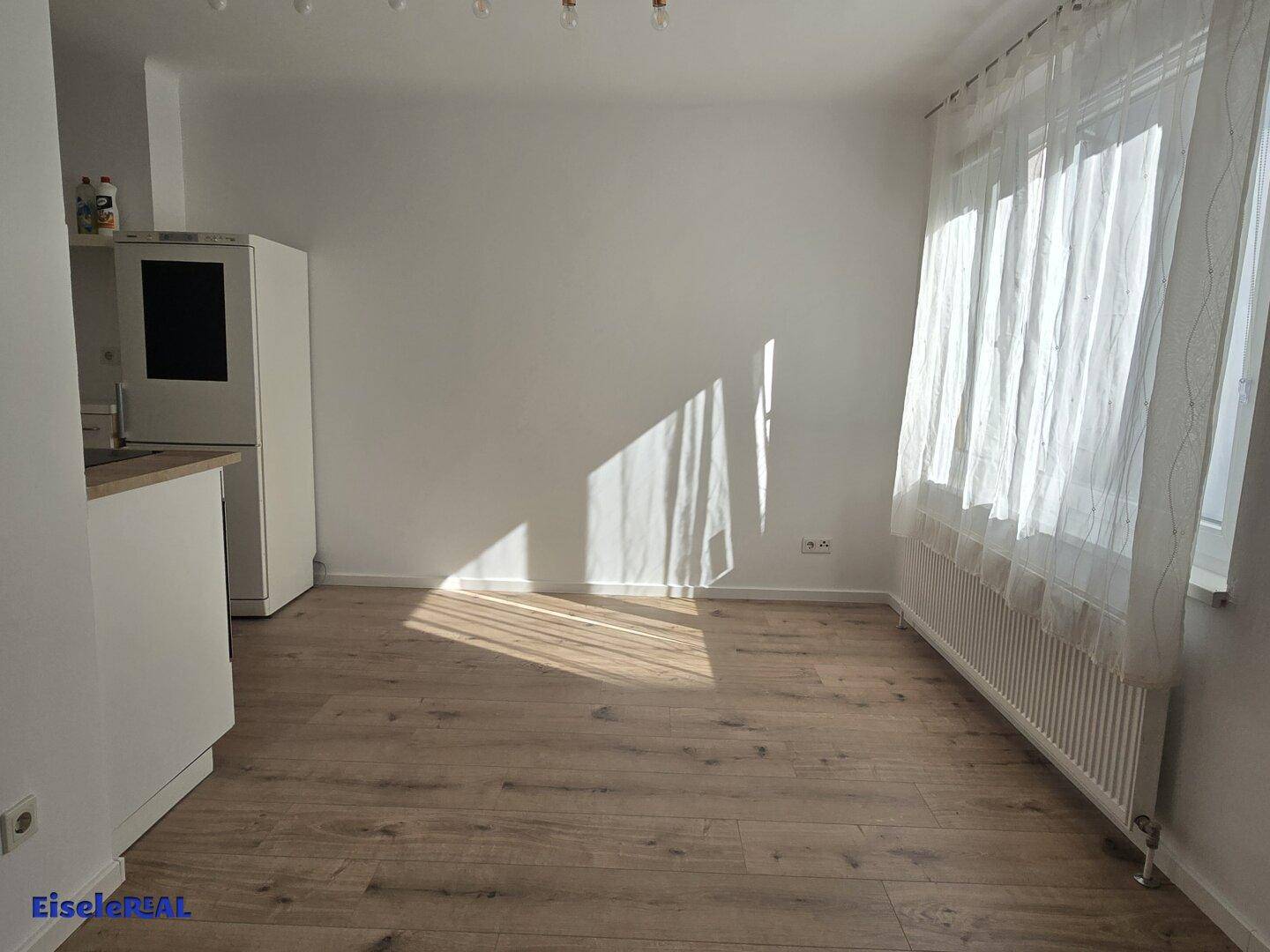 Heller Raum mit Laminatboden und viel Tageslicht, das durch das große Fenster einfällt.