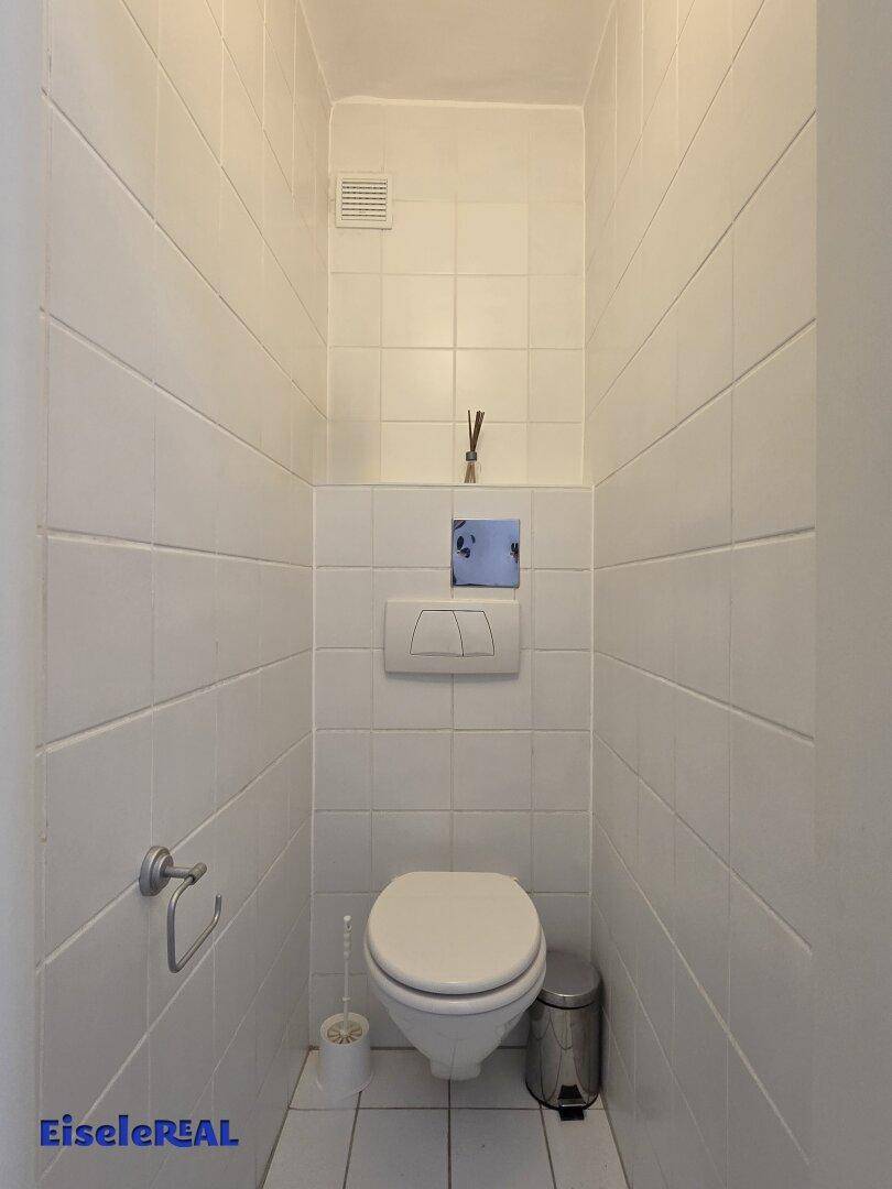 Kleines, gefliestes WC mit wandhängender Toilette und Deckenlüftung.