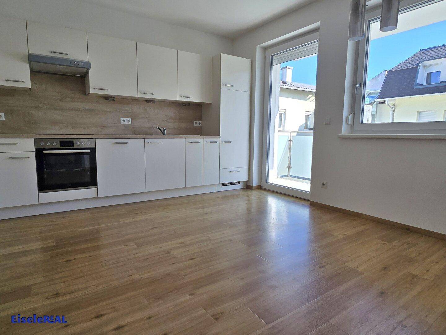 Heller Küchenbereich mit moderner Einbauküche, Holzoptik-Boden und Zugang zum sonnigen Balkon.