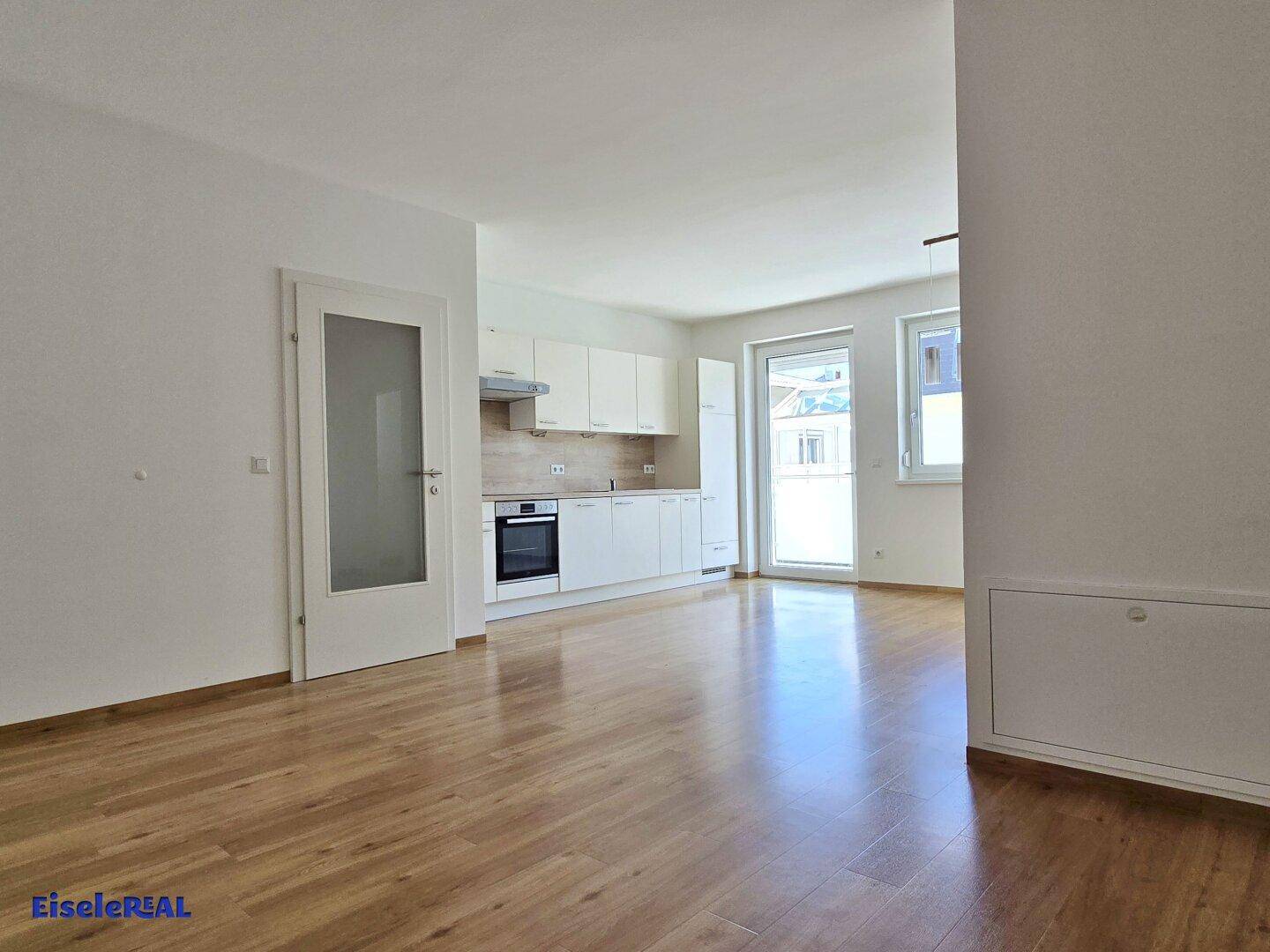 Offener Wohnbereich mit integrierter Küche, Laminatboden und viel Tageslicht, schafft ein helles Ambiente.