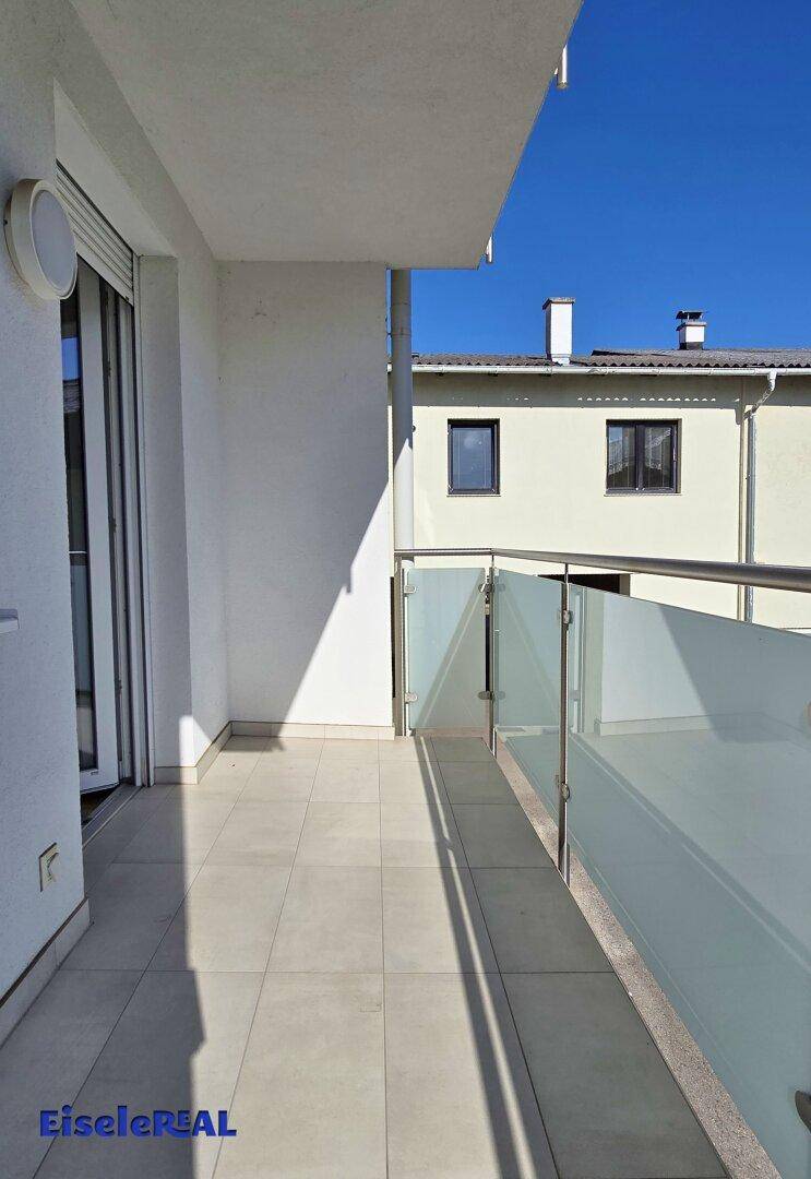 Heller Balkon mit Fliesenboden und modernem Glasgeländer, bietet einen angenehmen Ausblick auf die Umgebung.