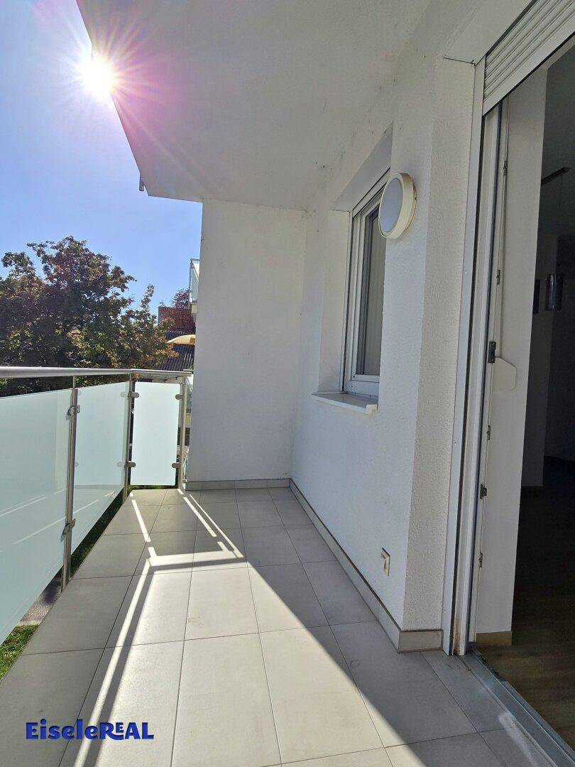 Sonniger Balkon mit Fliesenboden und Glasgeländer, ideal für entspannte Stunden im Freien mit Grünblick.